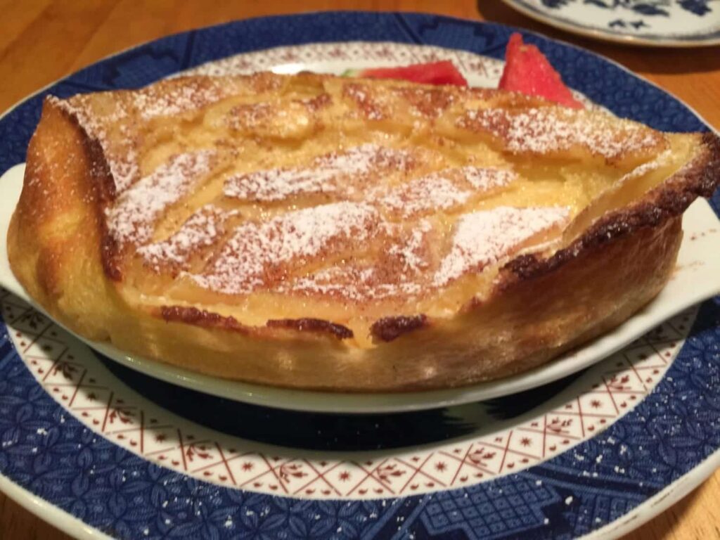 A golden-brown Dutch baby pancake dusted with powdered sugar on a blue and white patterned plate.