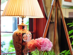 Another detail of the Gathering Room at the 1795 Acorn Inn Bed and Breakfast located in the Finger Lakes. Shown her is a ceramic lamp glazed in an oriental imari pattern. Fabulously fragrant and large pink peonies blossom next to the lamp. In the background stands an antique piece of surveying equipment used by the Innkeepers grandfather who was a bricklayer and helped build the Sears Robuck Tower in Chicago, IL.
