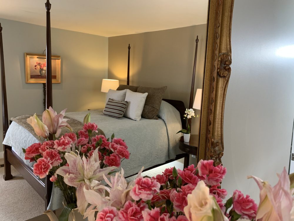 The Hotchkiss bed with a blue cotton damask quilt, blue and brown pillows, an oil paint and flowers as reflected in a gold framed mirror. The Hotchkiss Room at the 1795 Acorn Inn B & B is located on the first floor and has a private patio.