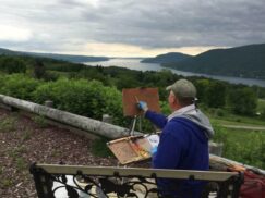 An artist painting plein air... sitting on a bench overlooking Canandaigua Lake on a moody day. This is part of the Plein Air Festival held annually in Canandaigua, Ontario County, NY